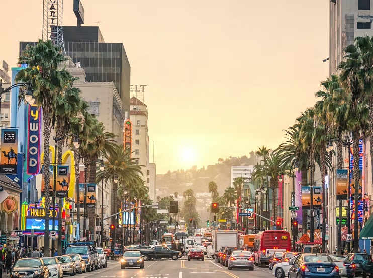 Hollywood street at sunset with palm trees and cars.